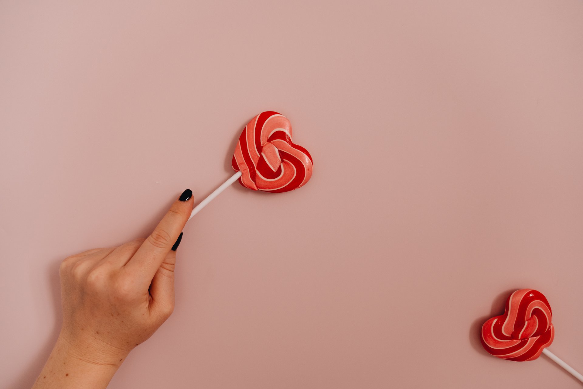 Hand-holding-a-lollipop-over-a-pink-background
